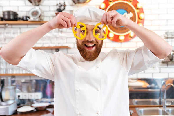 Cozinheiro chef engraçado olhando através de fatias de pimentão amarelo — Fotografia de Stock