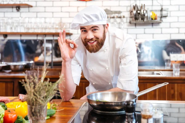 Neşeli sakallı Şef yemek pişirme ve ok işaret gösteren — Stok fotoğraf