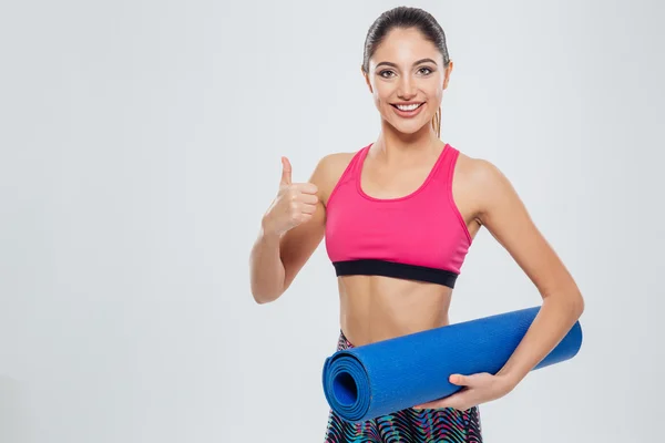 Mujer fitness sosteniendo esterilla de yoga y mostrando el pulgar hacia arriba —  Fotos de Stock