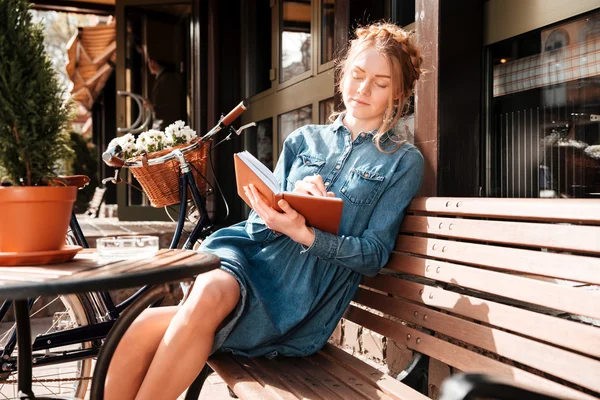 Mujer relajada sentada en el banco y escribiendo en un cuaderno — Foto de Stock