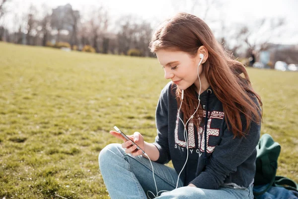 Smiling woman listening to musing from cell phone on lawn — Stock Photo, Image