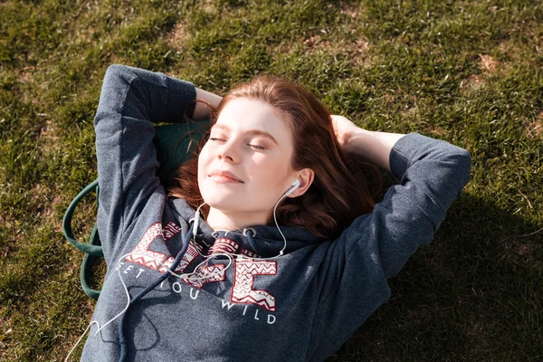 Heureuse femme détendue allongée sur l'herbe et écoutant de la musique — Photo