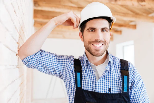 Sonriente constructor guapo de pie cerca de la pared —  Fotos de Stock