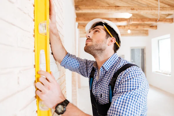 Builder in uniform holding a level against the wall indoors — стоковое фото