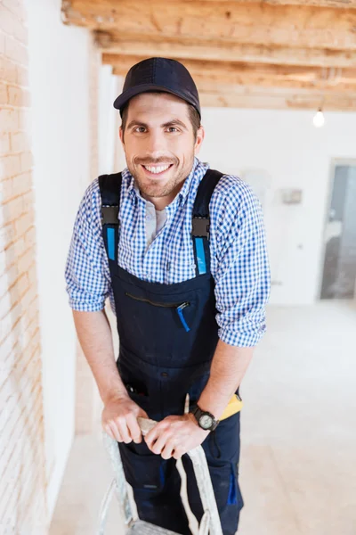 Веселый строитель улыбается и стоит на лестнице — стоковое фото