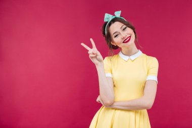 Gülümseyen barış işareti gösterilen sarı elbiseli çekici genç kadın