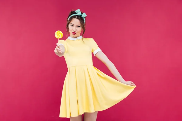 Lachende aantrekkelijke pinup meisje in gele jurk tonen zoete lollipop — Stockfoto