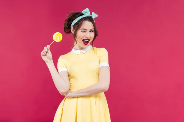 Cheerful charming pinup girl with yellow lollipop standing and w