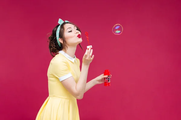 Mujer encantadora en vestido amarillo de pie y soplando burbujas de jabón —  Fotos de Stock