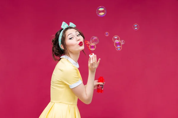 Giocoso carino pinup ragazza in abito giallo che soffia bolle di sapone — Foto Stock