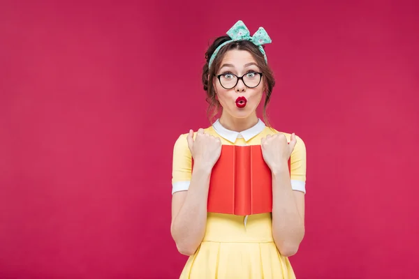 Surprised pinup girl in glasses standing and holding red book