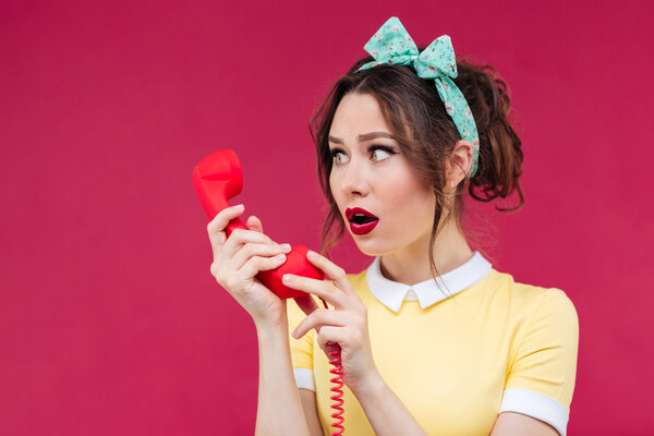 Удивлённая удивлённая молодая женщина разговаривает по телефону с красным приемником
