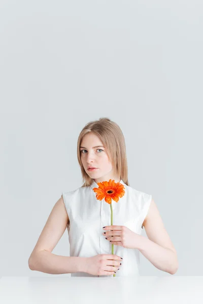 Mujer rubia sentada a la mesa y sosteniendo la flor — Foto de Stock