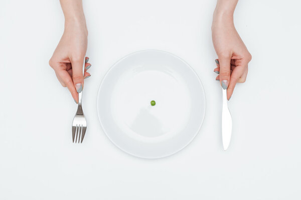 Woman eating one small green pea using knife and fork