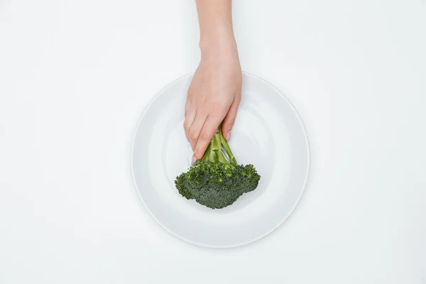 Вид сверху на руку женщины, кладущей брокколи на тарелку — стоковое фото