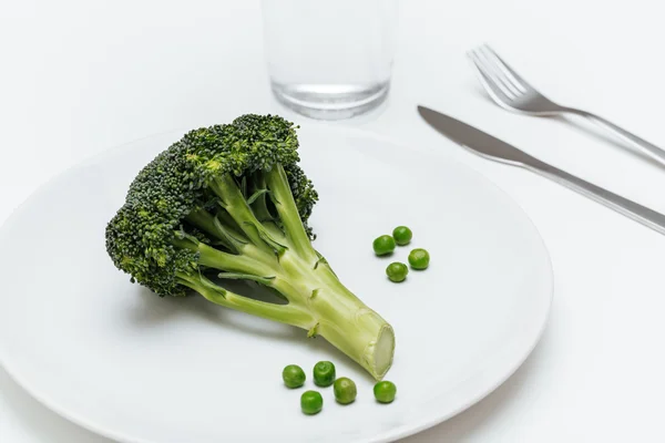 Bicchiere d'acqua, forchetta, coltello, piatto con piselli e broccoli — Foto Stock