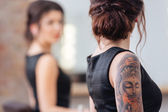 Žena s tetování na ruku stojící před zrcadlem
