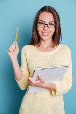 İşaret ve defter tutan mavi arka plan üzerinde gülümseyen güzel kız