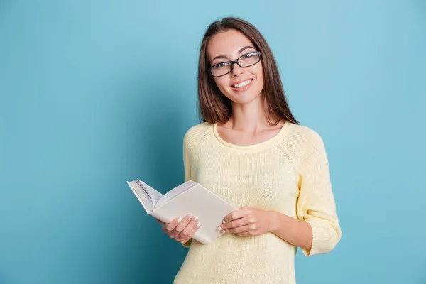 Jeune jolie fille avec des lunettes tenant livre sur fond bleu — Photo