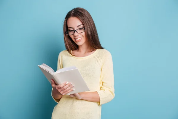 Молода дівчина читає книгу на синьому фоні — стокове фото