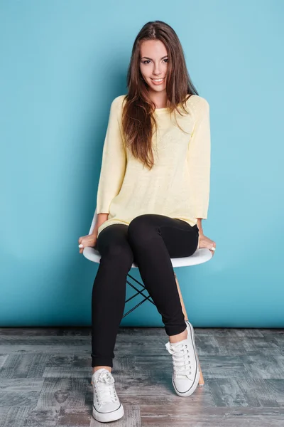 Pretty girl sitting on chair over blue background — Stock Photo, Image