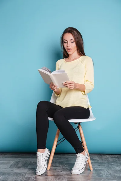 Nadenkend meisje lezen boek en zit op stoel — Stockfoto