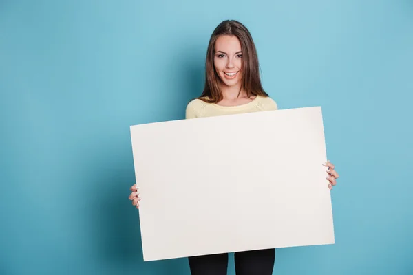 Pretty young woman holding empty blank board over blue background Stock Picture