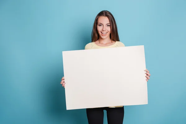 Pretty young woman holding empty blank board over blue background Stock Image