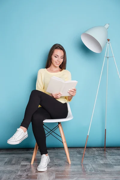 Güzel akıllı genç kadın sandalyede oturan kitap okuma — Stok fotoğraf