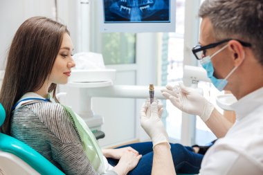 Erkek dişçi kadın hastasına diş implantı gösteriyor.