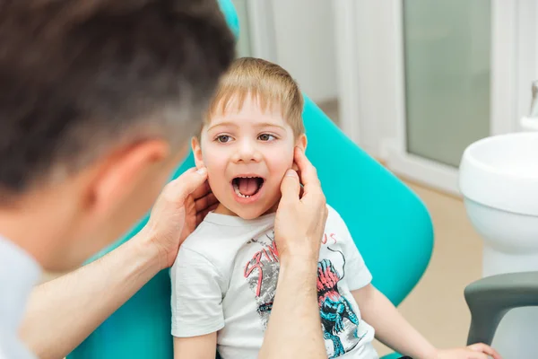 Dentista examinando los dientes de un niño sentado con la boca abierta — Foto de Stock