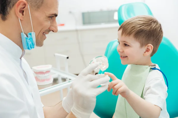 Hombre alegre dentista demostrando cepillado de dientes a niño pequeño — Foto de Stock