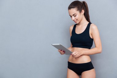 Güzel genç sporcumuz PC tablet gri bir arka plan üzerinde kullanma