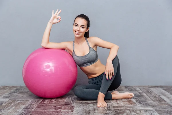 Joven hermosa chica de fitness con bola rosa mostrando signo de bien —  Fotos de Stock