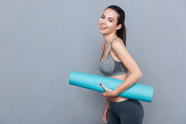 Attractive beautiful sportswoman holding yoga mat isolated over grey background — Stock Photo, Image