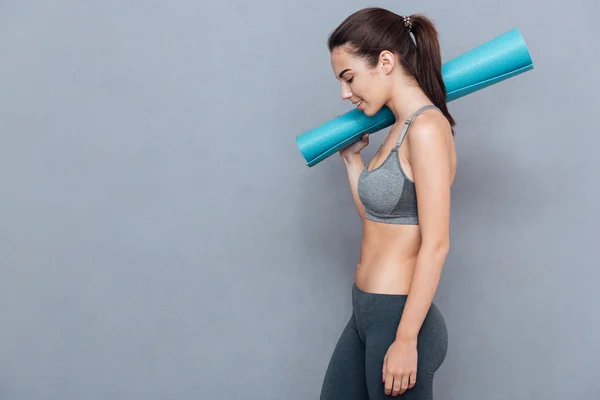 Cheerful beautiful fitness woman holding yoga mat and looking away — ストック写真