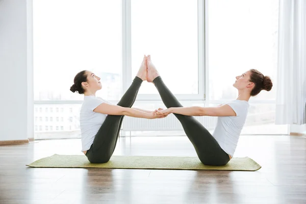 Due donne che allungano le gambe sul tappetino yoga verde — Foto Stock