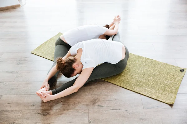 Two women stretching on the floor in yoga center