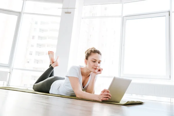 Vacker ung kvinna liggande på yogamattan och använder tablet — Stockfoto