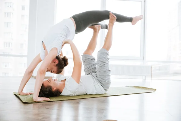 Sorridente giovane coppia che fa acrobatica posizione yoga in studio insieme — Foto Stock