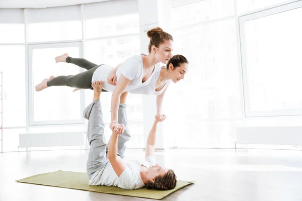 Ryhmä kaksi nuorta naista ja mies tekee acro jooga — kuvapankkivalokuva