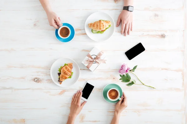 Руки мужчины и женщины едят круассаны с кофе — стоковое фото