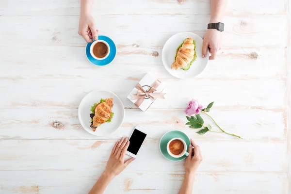 Руки мужчины и женщины пьют кофе, используя мобильный телефон — стоковое фото