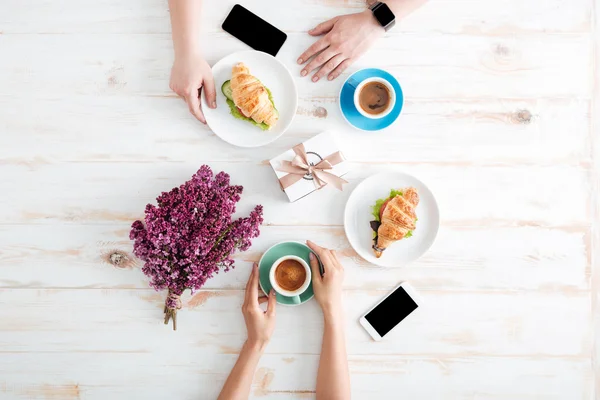 Руки пары пьют кофе и едят круассаны на столе — стоковое фото