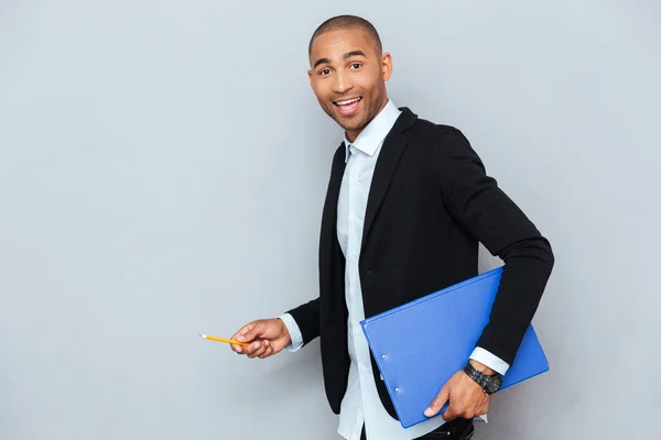 Feliz joven empresario caminando sosteniendo carpeta azul y lápiz — Foto de Stock