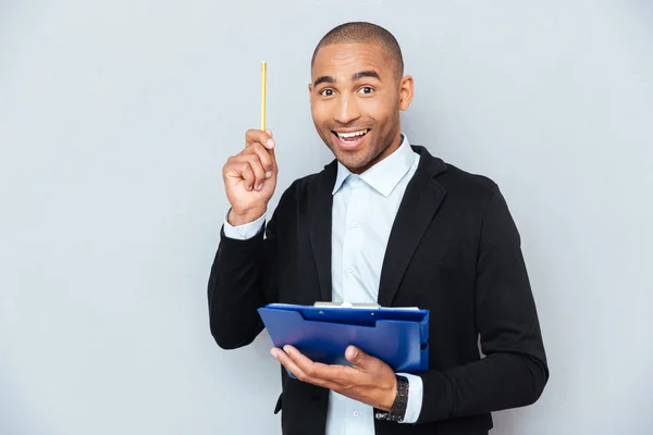 Glücklicher afrikanischer Mann mit Klemmbrett, das nach oben zeigt und eine Idee hat — Stockfoto