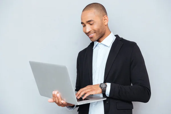 Sorrindo afro-americano jovem de pé e usando laptop — Fotografia de Stock