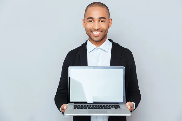 Sonriente joven afroamericano sosteniendo la computadora portátil de pantalla en blanco —  Fotos de Stock