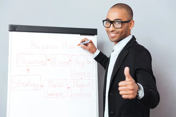Happy african man writing on flipchart and showing thumbs up — Stock Photo, Image