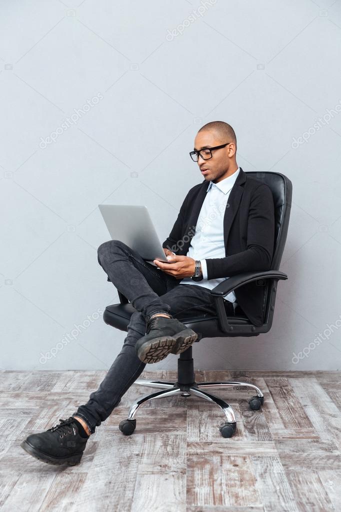 Concentrated young man sitting in office chair and using laptop